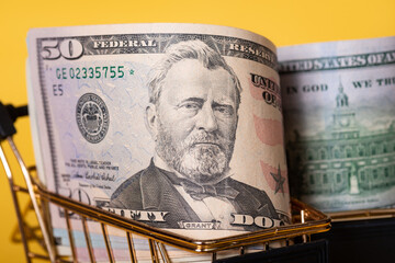 American banknotes dollars in a shopping cart on a yellow background. Shopping, discounts.