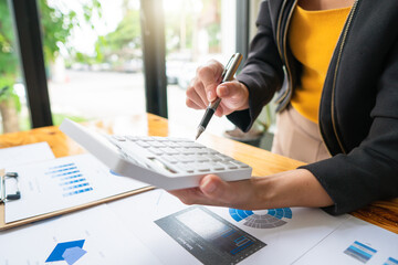 Close up hand of businessman or accountant hand holding pen working on calculator to calculate business data, accountancy document and laptop computer at office, business concept.