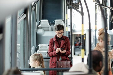 Obraz premium High angle view at adult woman using smartphone in bus while traveling by public transport in city, copy space