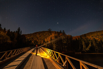 Woman with lantern under starry sky at the bridge over mountain river.