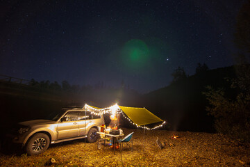 Tourist camping at the river bank at night under starry sky.
