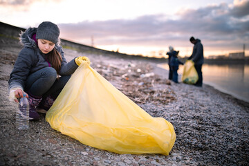 Preteen girl cleaning polluted sea shore from plastic garbage with her family