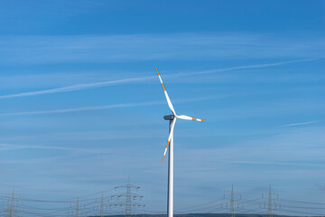 Wind turbine with three arms for electricity production standing in West Germany with a blue sky background.