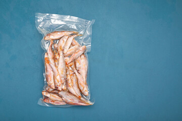 Frozen fish Mullus barbatus (red mullet) in transparent pack on blue background. Goatfish found in Mediterranean Sea, Black Sea and eastern North Atlantic Ocean. Top view, copy space