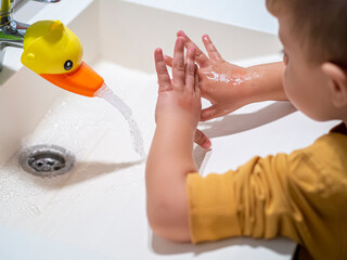 Kid washing hands in a bathroom sink at home after playing with duck toy as a faucet. Fun faucet...