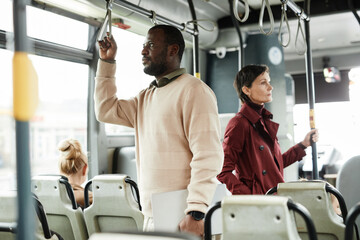 Side view portrait of African-American man holding onto railing in bus while traveling by public transport in city, copy space