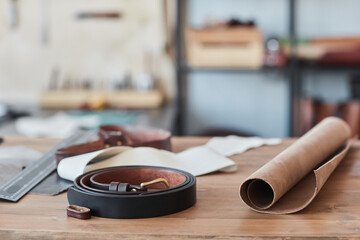 Close up background image of handmade leather belt on wooden table in artisan workshop, copy space