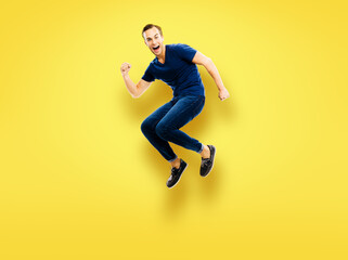 Fototapeta na wymiar WOW! Unbelievable news, sales or discounts concept - full body studio image of jumping in air excited, shocked astonished surprised very happy man in blue cloth, isolated on yellow background.