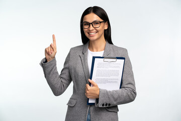 Waist up portrait view of the business lady wearing eyeglasses and office suit holding clipboard and pointing up with her finger isolated over white background