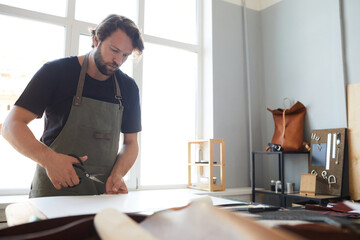 Portrait of male artisan cutting leather while working in tanner workshop, copy space