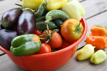 A set of fresh vegetables from your garden. Eggplant, pepper, tomatoes, cucumbers in a red bowl on a wooden background.