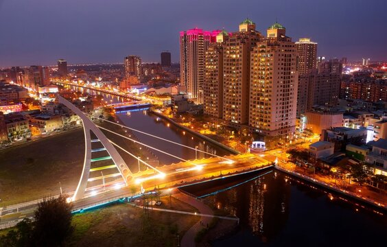 Night skyline of high-rise riverside buildings in Anping District, Tainan City, Taiwan, with a cable stayed bridge across the canal and city lights dazzling under blue twilight sky