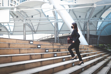 A business woman wearing a suit jacket and trousers is walking up stairs outdoors.