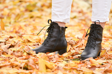 Close-up  girl's legs in black fashion boots on fallen yelllow leaves , autumn leather shoes  