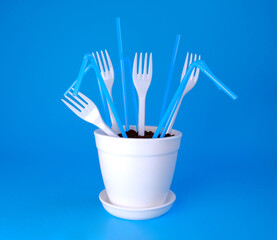 Forks and straws in a white pot on a blue background. Plastic in the ground