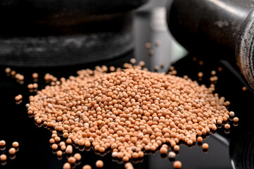 Yellow mustard seeds with a mortar on reflective black background.  Selective focus ; macro. 