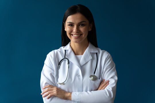 Portrait photo of attractive friendly family doctor wearing white lab coat and stethoscope smiling friendly and posing arms crossed isolated blue color background