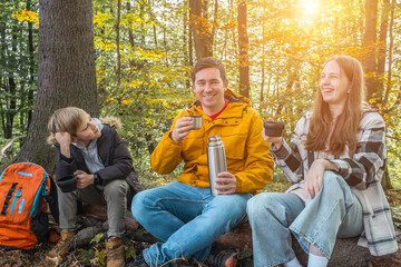 Hikers Father, daughter and son resting in nature forest, drinking hot tea thermos in sunny autumn day, Fall wood. Contemporary Travel. Yellow, orange, ocher colour. Family vacation.