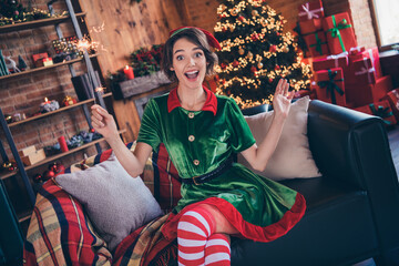 Photo of amazed shocked joyful woman santa helper sit couch christmas mood spirit sparkler indoors inside house home