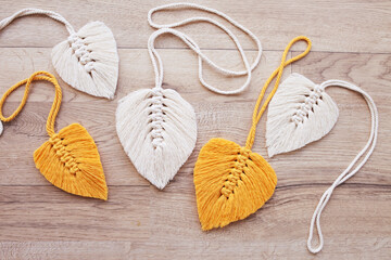 Macrame leaves in yellow  and natural color on the wooden background. Cotton rope decor macrame to make your home more cozy and unique.