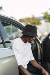 Chico negro atlético en coche con puerta abierta posando con ropa urbana