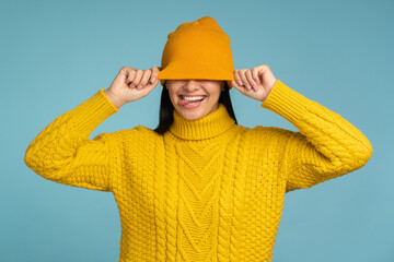 Caucasian woman feeling great during freezing weather wearing yellow sweater and warm hat and showing tongue with funny mood