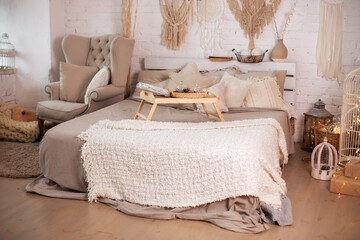 Wooden breakfast tray on bed. Cozy christmas decorated bedroom scandinavian interior with armchair and comfortable bed with a small table on bed and pillows, copy space. concept new year and holidays.