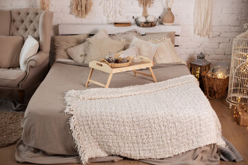 Wooden breakfast tray on bed. Cozy christmas decorated bedroom scandinavian interior with armchair and comfortable bed with a small table on bed and pillows, copy space. concept new year and holidays.