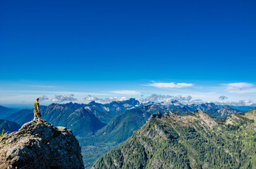 An athletic adventurous male hiker standing on top of a mountain looking out at a mountain range.