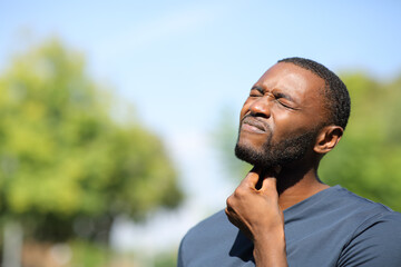 Man with black skin suffering sore throat in a park - obrazy, fototapety, plakaty