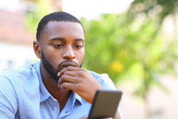 Worried man with black skin checking mobile phone in a park