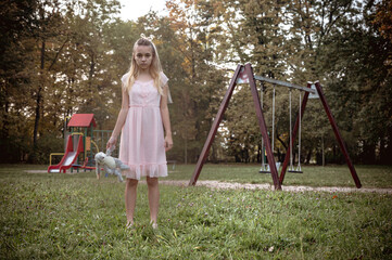 Ghost teen girl in white dress with dirty toy near an empty playground. Holiday event halloween...