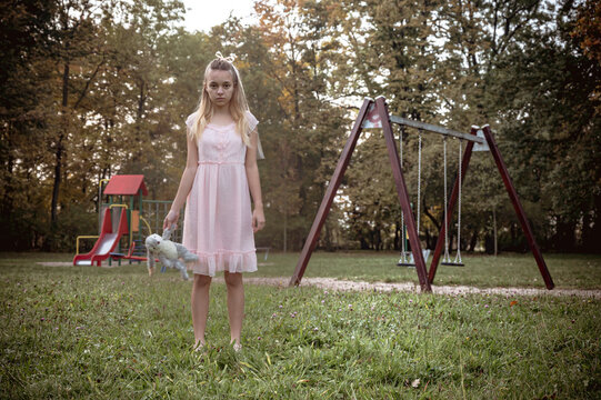 Ghost teen girl in white dress with dirty toy near an empty playground. Holiday event halloween concept.