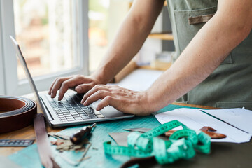 Close up of unrecognizable male artisan using laptop while working in tanners workshop, copy space