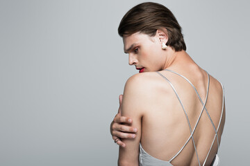 transgender woman in slip dress and earring touching hand while posing isolated on gray