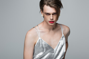 young transgender man with makeup posing in slip dress isolated on grey