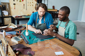 Portrait of male artisan teaching young apprentice using wheelchair in leatherworkers workshop, copy space - obrazy, fototapety, plakaty
