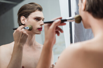 young transgender man applying face powder near mirror