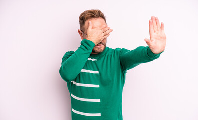 middle age handsome man covering face with hand and putting other hand up front to stop camera,...