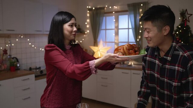 asian woman serving Christmas turkey dish in plate and letting her husband smell the aroma while they are getting ready for festive dinner at home