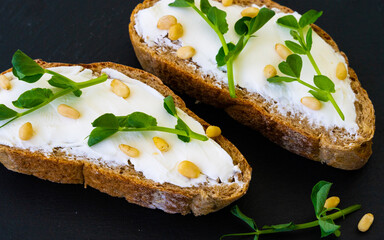 Bran bread with cream cheese and microgreen peas and pine nuts on a black slate board. Healthy eating. Superfood.
