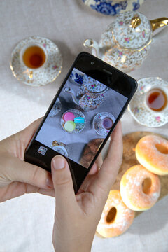 Top view picture of lady,blogger sitting in cafe and making photo with mobile of food, afternoon tea with doughnuts and macarons on the table high angle, food and social media concept