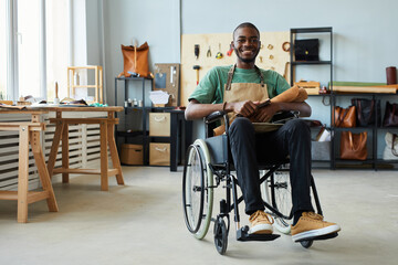 Full length portrait of smiling African-American man using wheelchair enjoying work in...