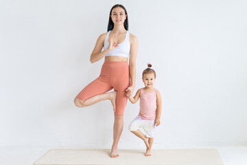 Young attractive mother meditates with her little daughter. Balance exercise. Couple yoga.
