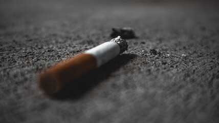 lit cigarette with burned ashes lying on concrete with heavy bokeh