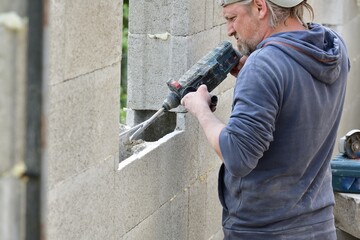 Worker building a wall on a house and drilling into a wall with manual drill