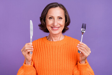 Photo of attractive senior woman hold metal cutlery ready to eat starving isolated over purple...