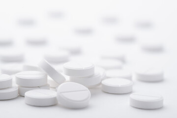 A pile of white pills scattered on a bright white background. Selective focus.