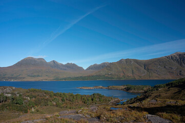 Views over forest and Loch Torridon to Beinn Alligin and Liathach mountains on a sunny day. Blue sky and light cloud with jet stream. No people.