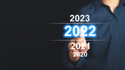 Welcome to the happy new year in 2022. Businessman in blue shirt pointing to digital 2022 calendar while standing with a black background in the studio. Business startup or goal to success